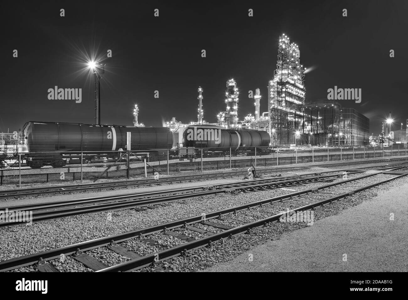 Illuminata raffineria di petrolio a notte con binari in primo piano, il porto di Anversa, Belgio. Foto Stock