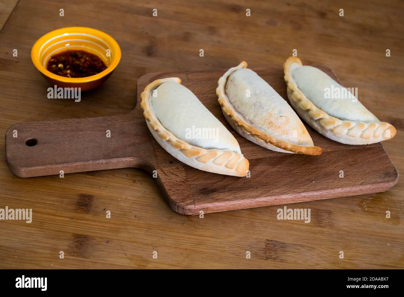 Empanadas argentini al forno tradizionale, dolci salati con ripieno di carne di manzo o verdure su sfondo di legno e salsa piccante. America Latina Foto Stock