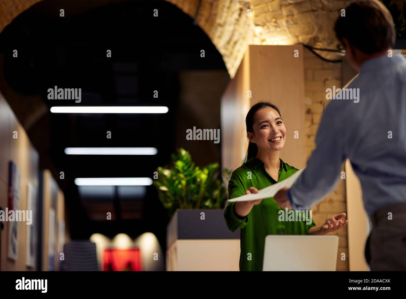Giovane allegra donna asiatica che dà alcuni documenti al suo collega e sorridendo mentre si sta insieme nell'ufficio moderno. Uomini d'affari e concetto di lavoro Foto Stock