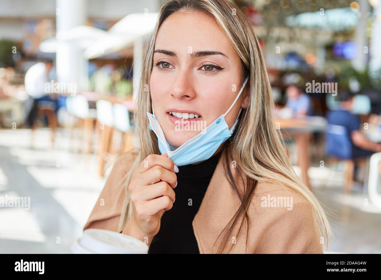 Donna con maschera viso sul mento con caffè per andare in una caffetteria nel centro commerciale Foto Stock