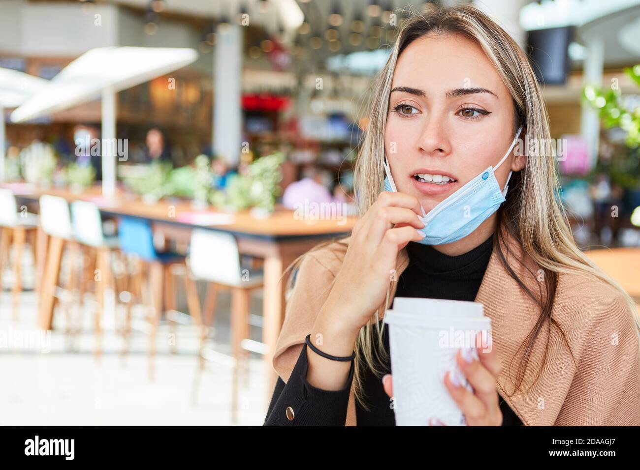 Giovane donna come ospite nel centro commerciale con un caffè per andare tazza e una maschera per il viso il mento Foto Stock