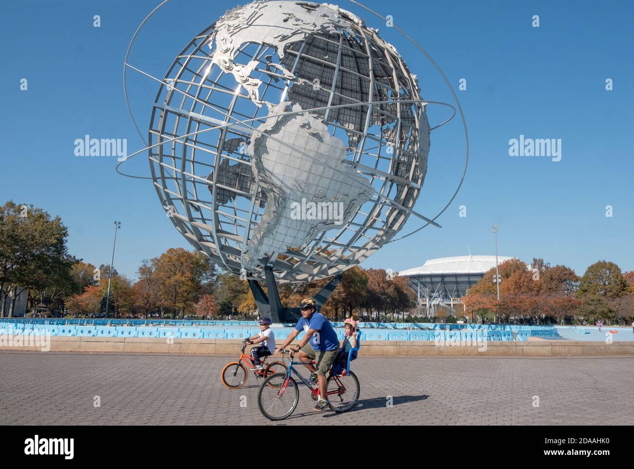 In un dolce giorno d'autunno, una famiglia bike intorno al perimetro dell'Unisfero in Flushing Meadows Corona Park a Queens, New York City Foto Stock