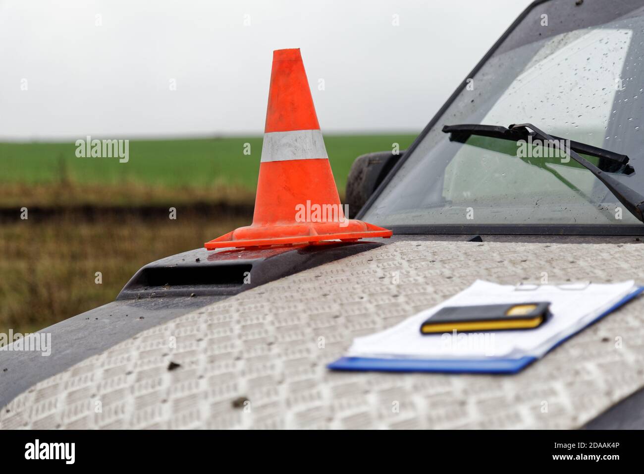 Cono stradale arancione con striscia bianca sul cofano di un veicolo per il servizio stradale. Clip per supporto carta per Appunti e telefono in primo piano sfocato. Poco profondo Foto Stock