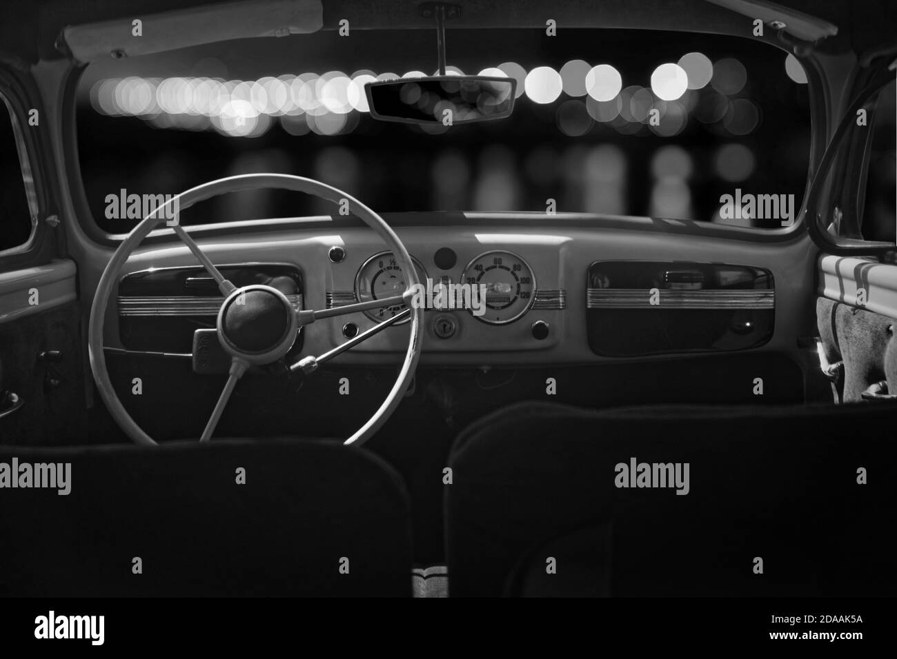 Vecchia cabina, console e volante in un'auto d'epoca retrò. Luci notturne. Immagine in bianco e nero. Foto Stock