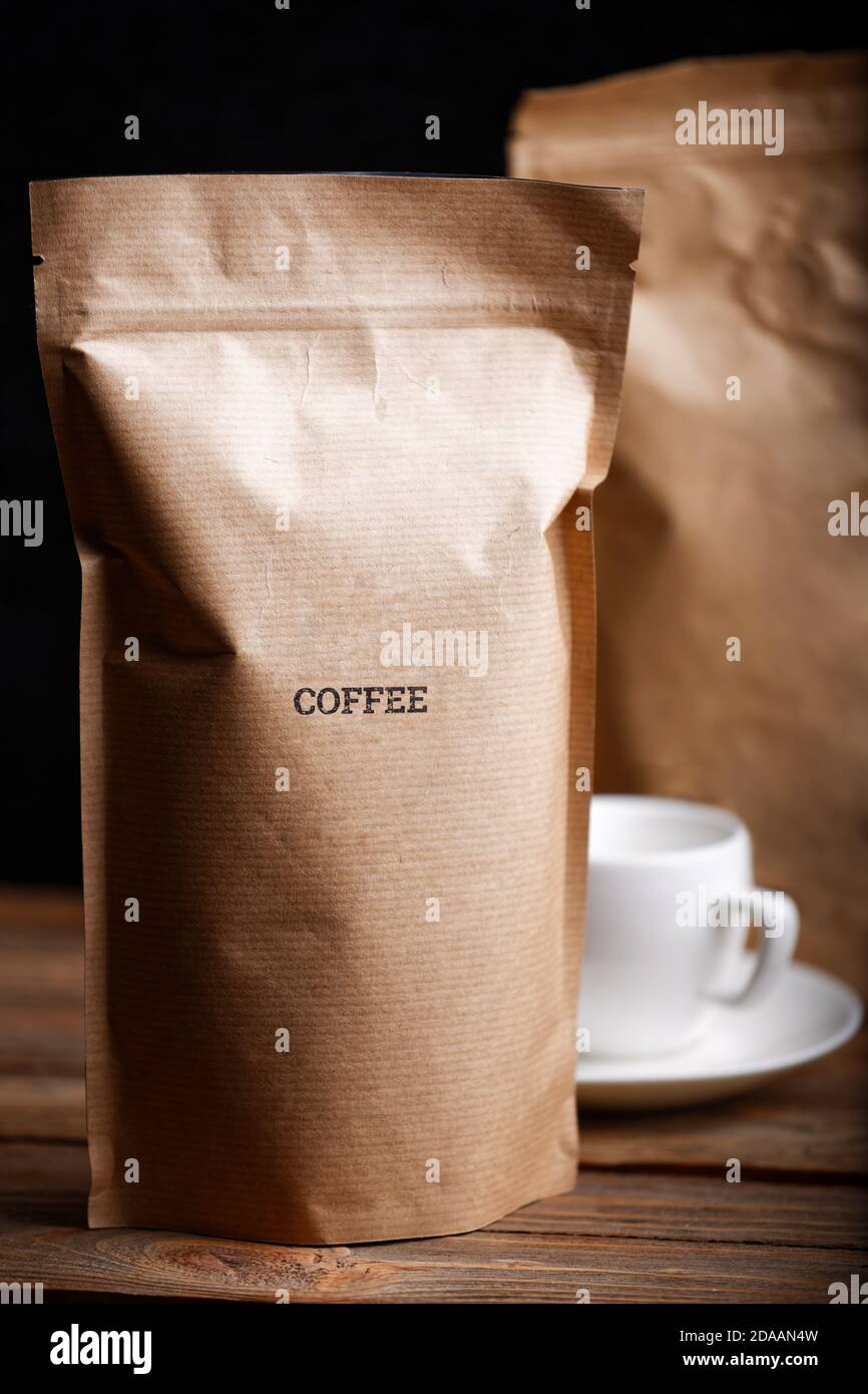 Sacchetti di carta artigianali marroni con chicchi di caffè su tavolo di legno su sfondo nero Foto Stock