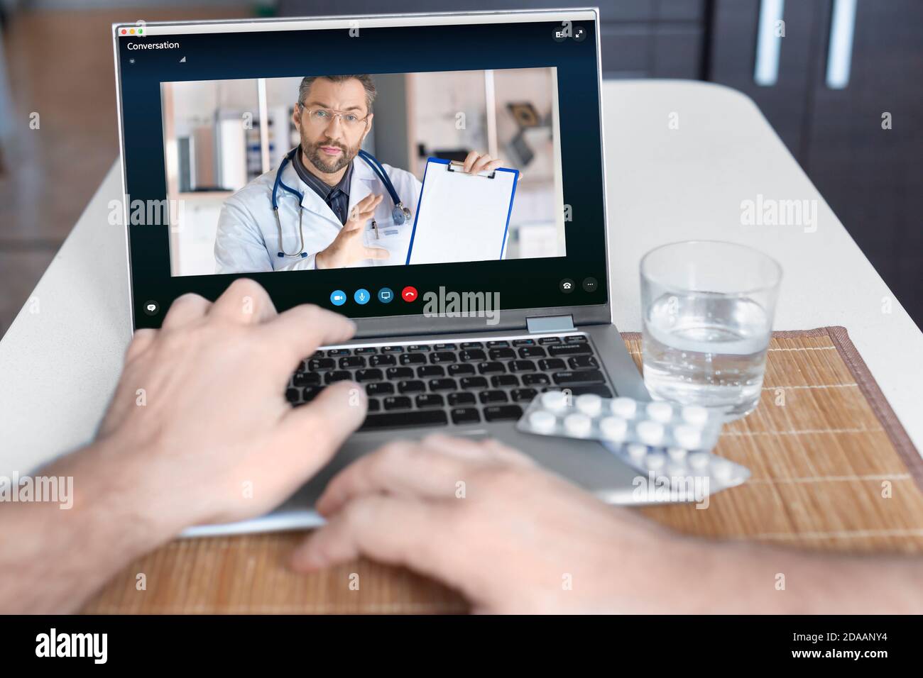 Una vista ravvicinata della mano di un paziente davanti a un computer portatile durante una consultazione online con un medico. Medico spiega al paziente la prodeu Foto Stock