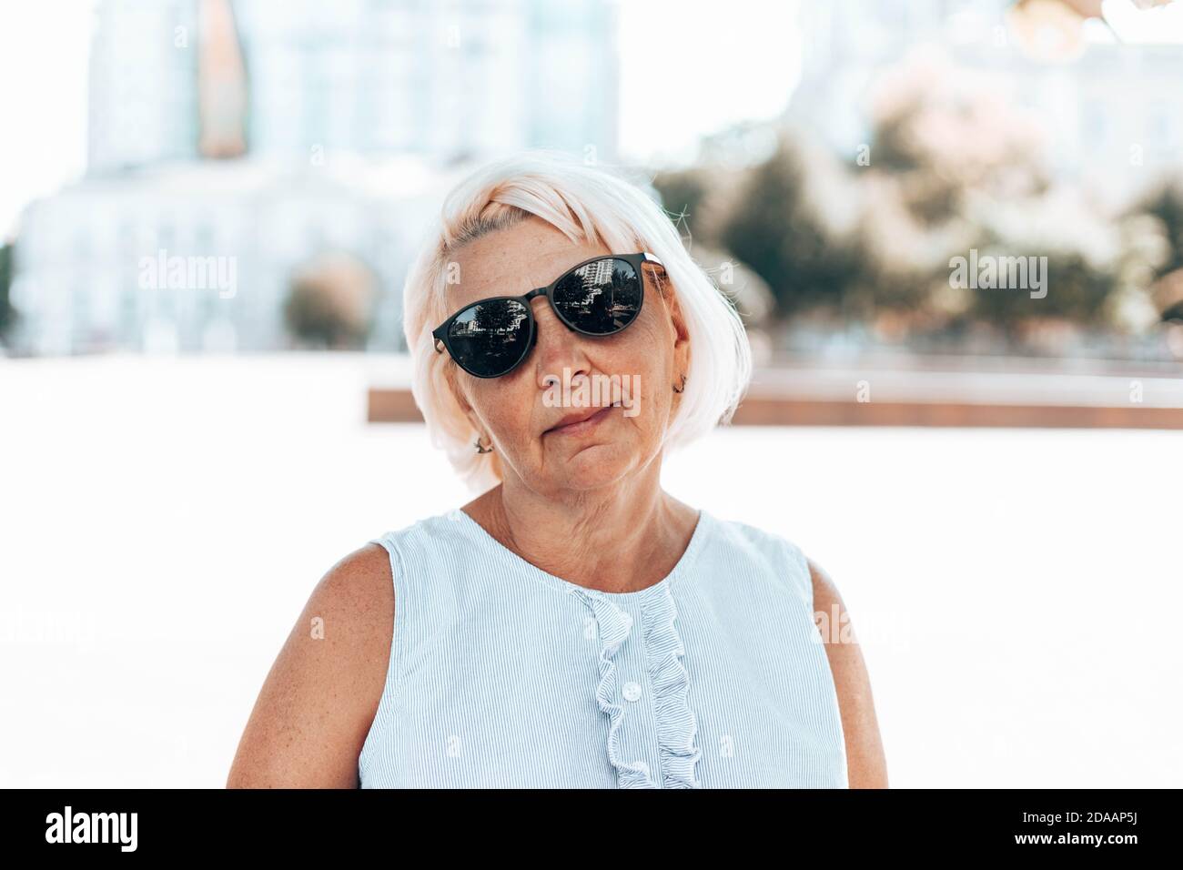 Ritratto di bionda positivo soddisfatta donna matura in occhiali da sole sguardi alla telecamera all'aperto nel parco Foto Stock