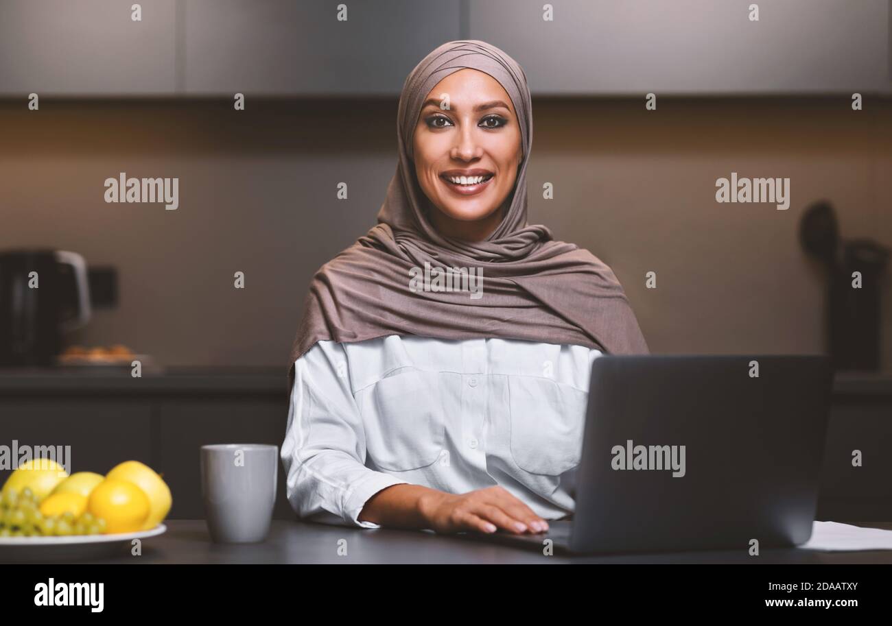 Allegra donna araba al computer portatile che lavora online a casa Foto Stock