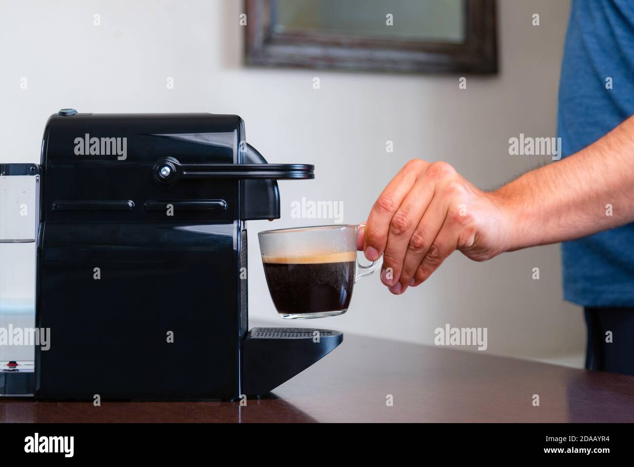 Primo piano di una mano che raccoglie una tazza di caffè espresso con macchina da caffè a capsule a casa. Concetto di pausa caffè. Foto Stock