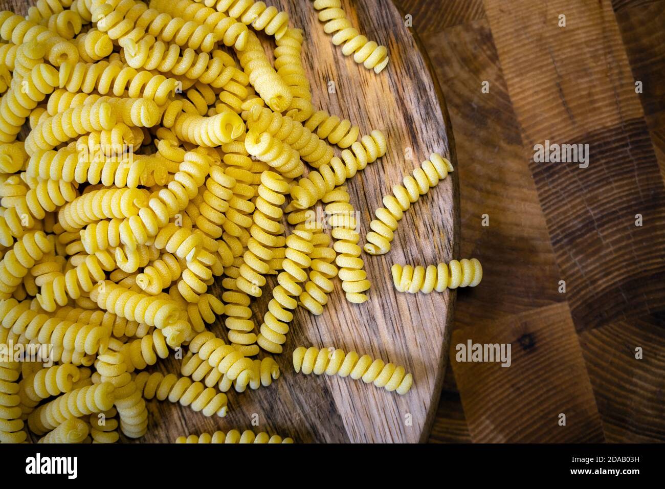 Pasta arricciata non cotta su fondo tavola di legno. Pila di tradizionali maccheroni crudi secchi. Nessuno Foto Stock