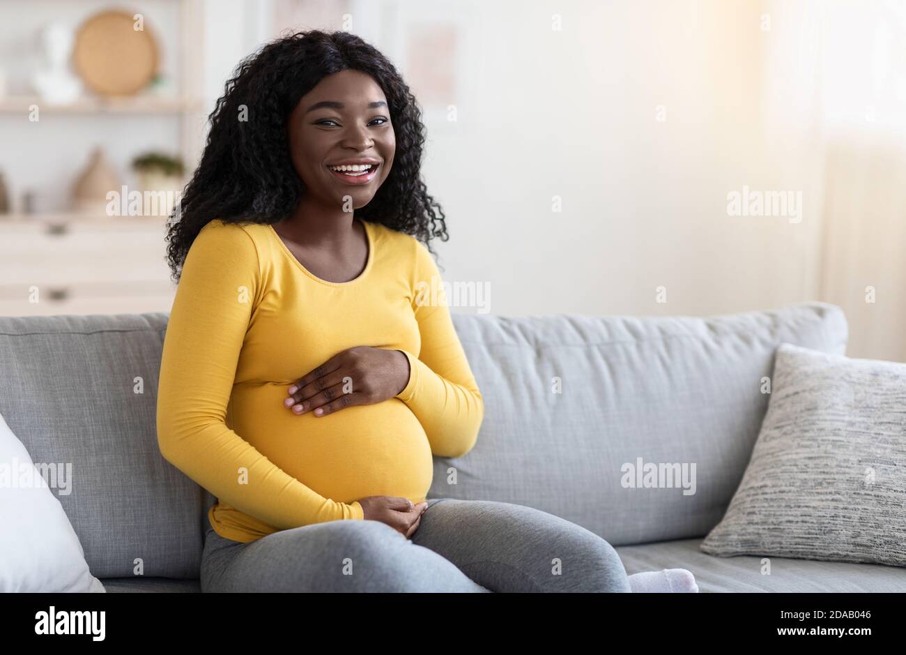 Gioiosa donna nera incinta abbracciando la sua grande pancia Foto Stock