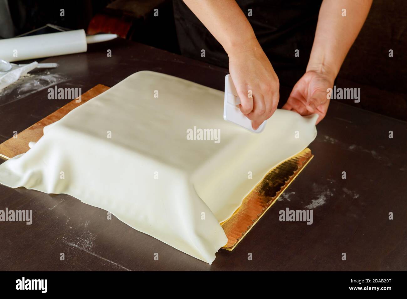 Donna che decora torta quadrata con fondente bianco. Tecnica di fare torta di nozze. Foto Stock