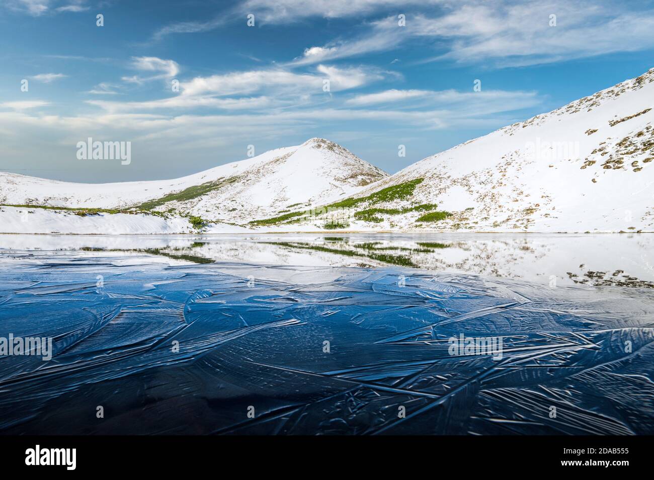 Lago di montagna ghiacciato con ghiaccio blu e crepe sulla superficie. Pittoresco paesaggio invernale con colline innevate sotto un cielo blu, montagne Carpazi, Europa Foto Stock