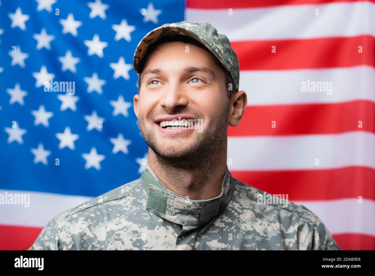 allegro militare uomo in uniforme e cappello sorridente vicino americano contrassegno su sfondo sfocato Foto Stock