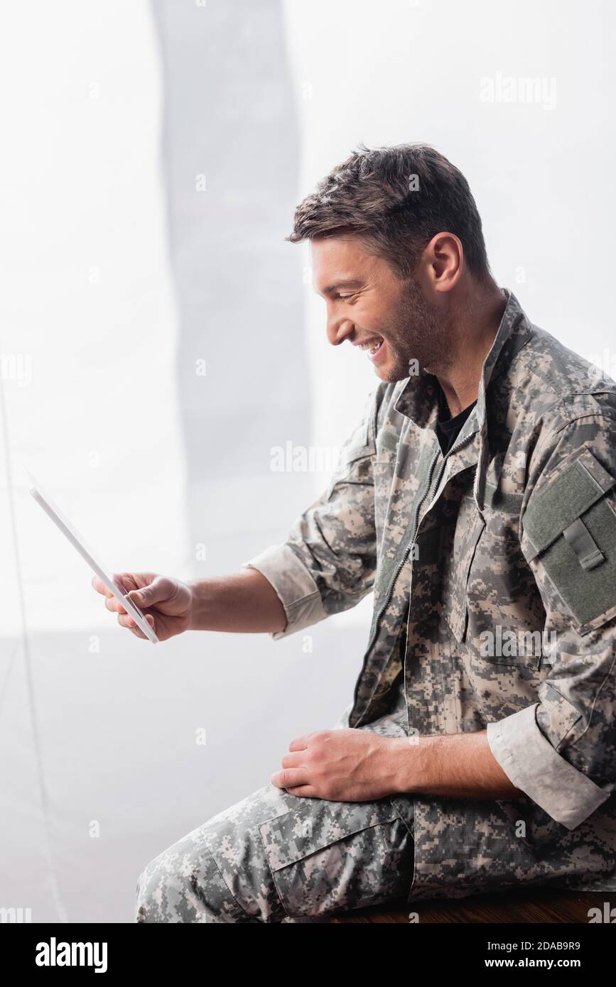 un soldato allegro in uniforme militare che utilizza un tablet digitale in ufficio Foto Stock
