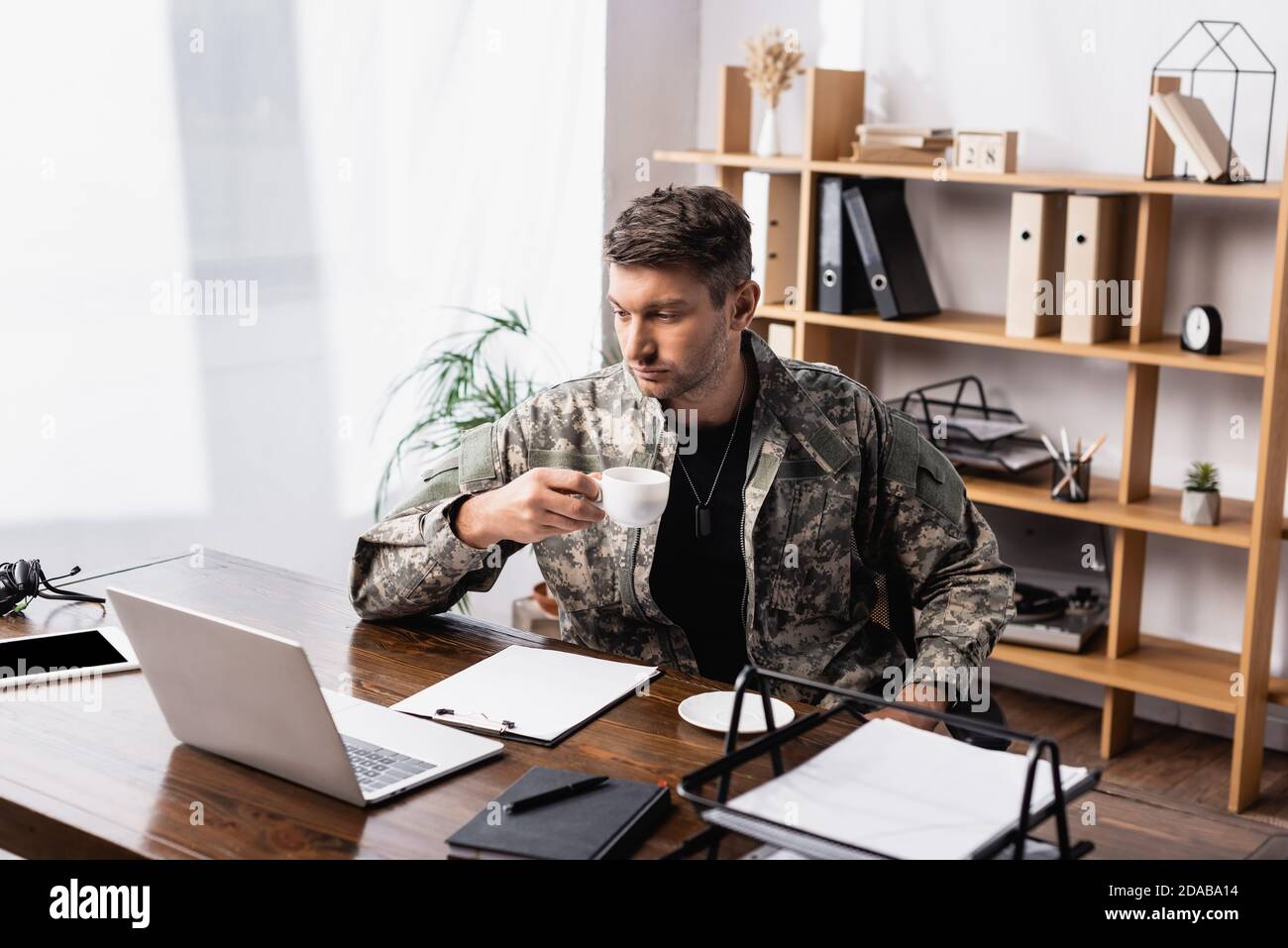 uomo militare in uniforme che tiene la tazza mentre si guarda il laptop Foto Stock