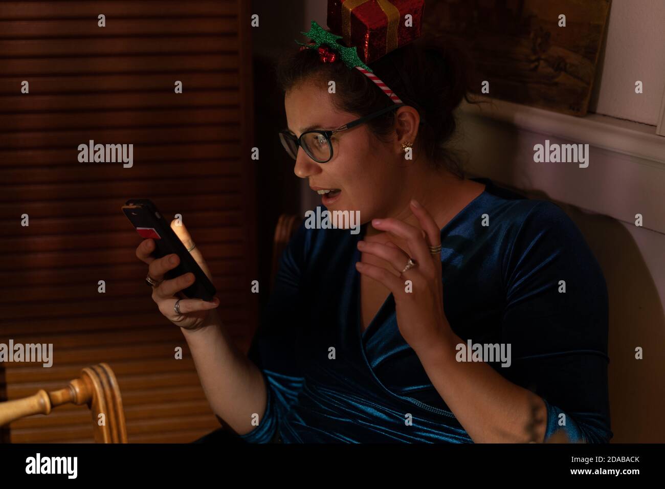 Sorpresa giovane donna con decorazione dei capelli di natale guardando nel suo telefono a natale. Foto Stock