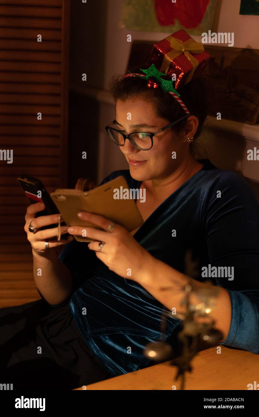 Donna giovane nerdy con capelli decorati che guarda addicted in due telefoni cellulari a Natale. Foto Stock