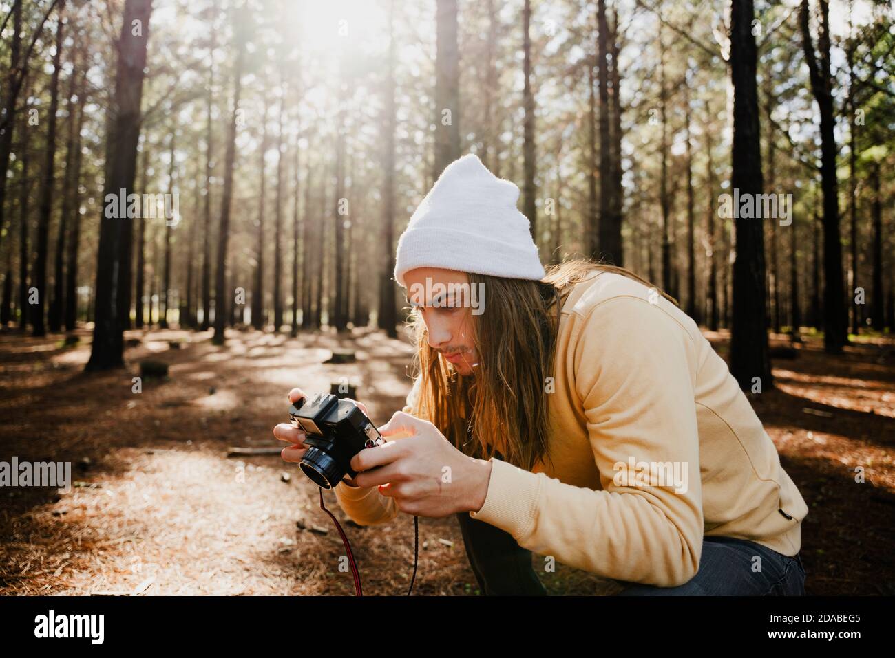 Teen photographer caucasico che scatta le foto per il progetto della scuola che si accovaccia dentro boschi verdi Foto Stock