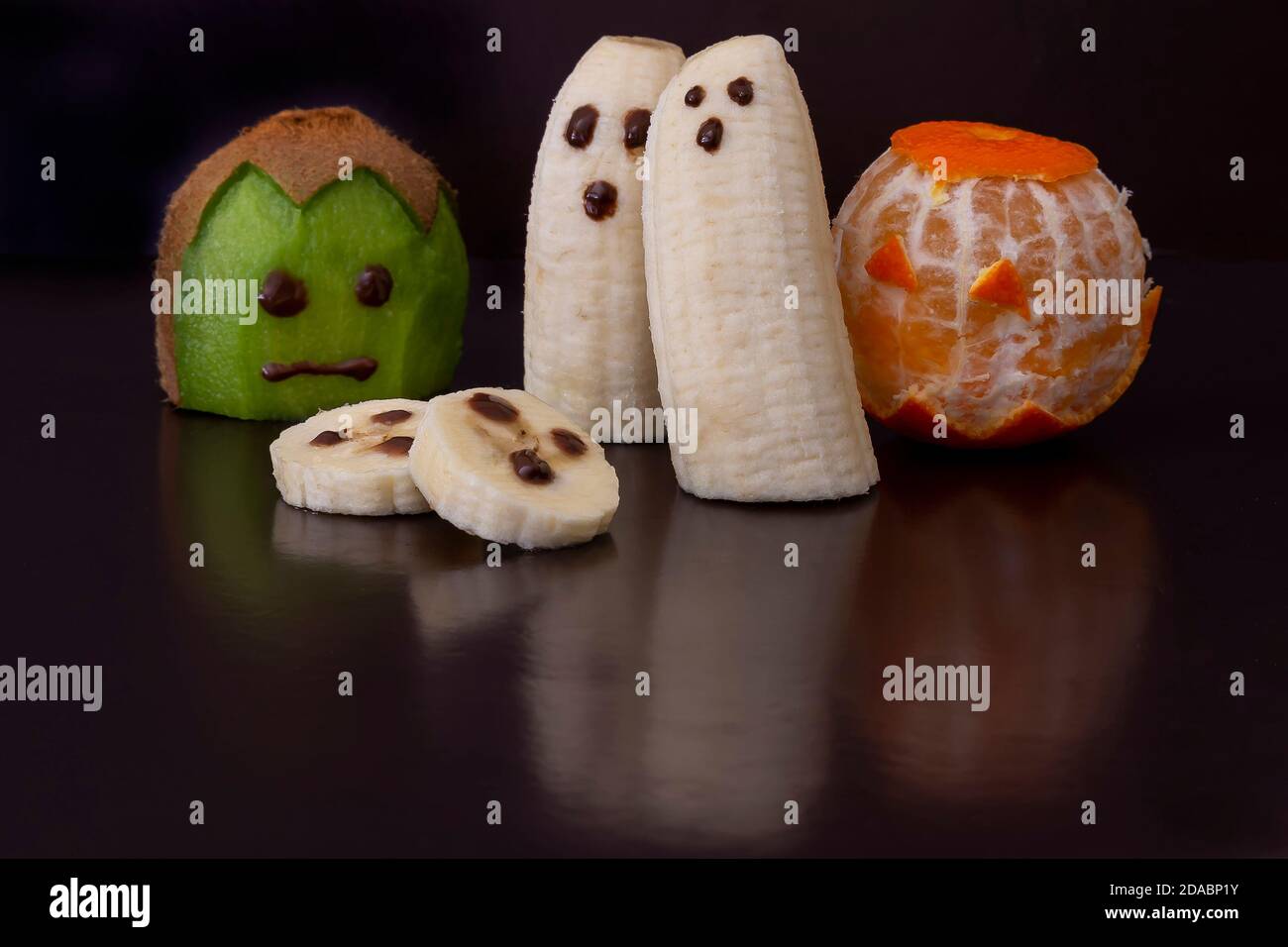 Piccoli simpatici mostri e fantasmi in stile halloween realizzati con taglio frutta e decorata su sfondo nero lucido riflettente Foto Stock