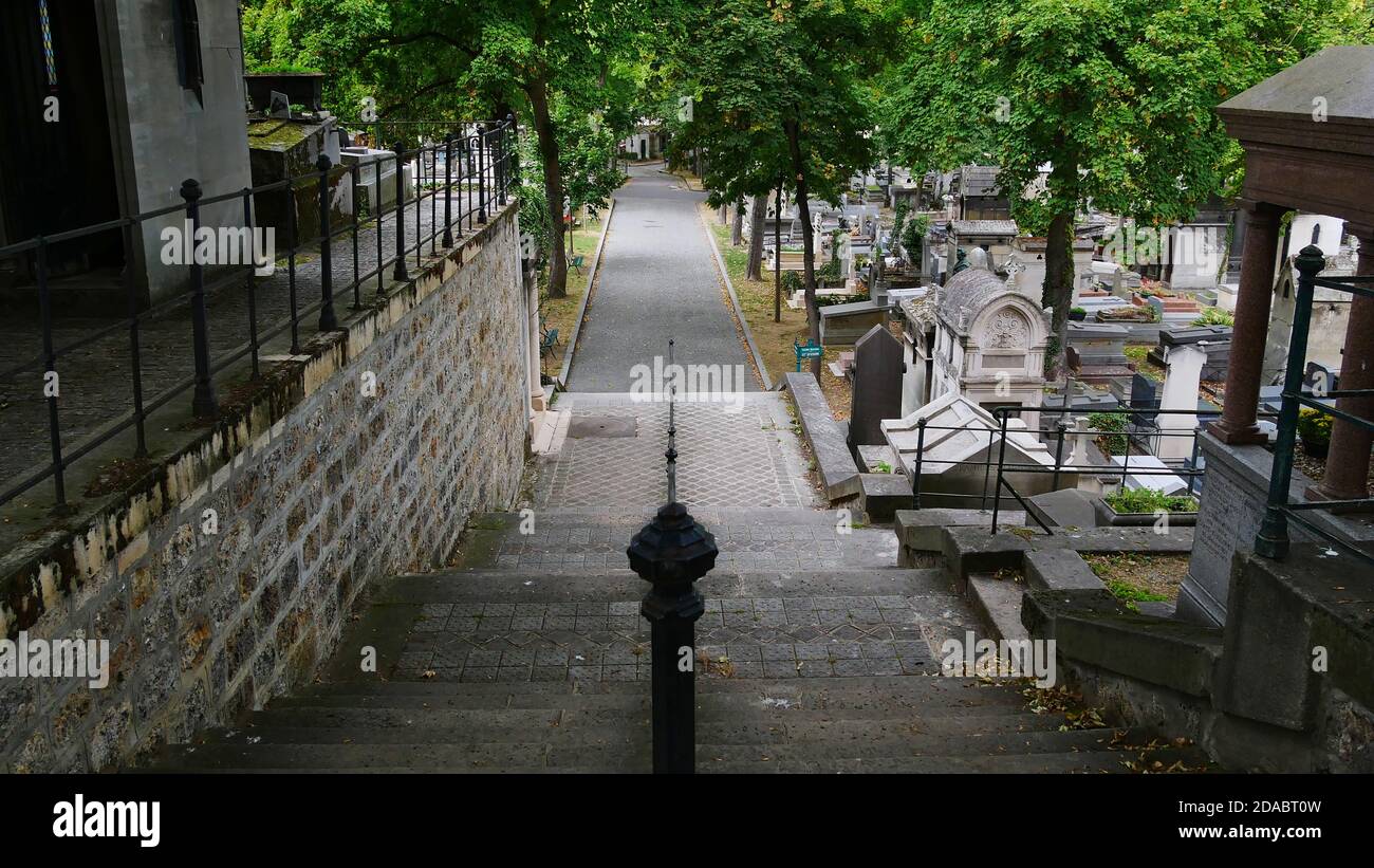 Parigi, Francia - 09/08/2019: Vista tranquilla sul bellissimo cimitero di Montmartre con scale, sentiero lastricato, ringhiera metallica, tombe e alberi verdi. Foto Stock