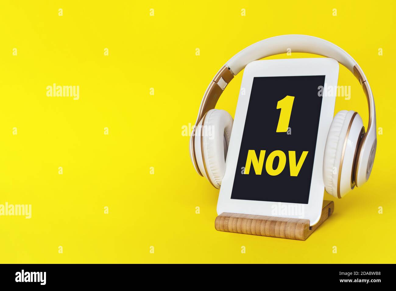 1 novembre . Giorno 1 del mese, data del calendario. Cuffie eleganti e moderno tablet su sfondo giallo. Spazio per il testo. Istruzione, tecnologia, vita Foto Stock