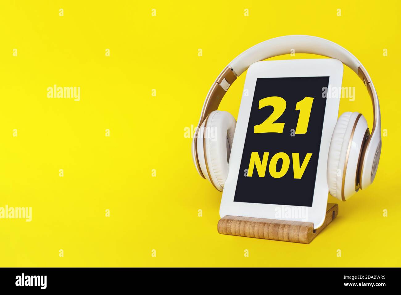 21 novembre . Giorno 21 del mese, data del calendario. Cuffie eleganti e moderno tablet su sfondo giallo. Spazio per il testo. Istruzione, tecnologia, vita Foto Stock