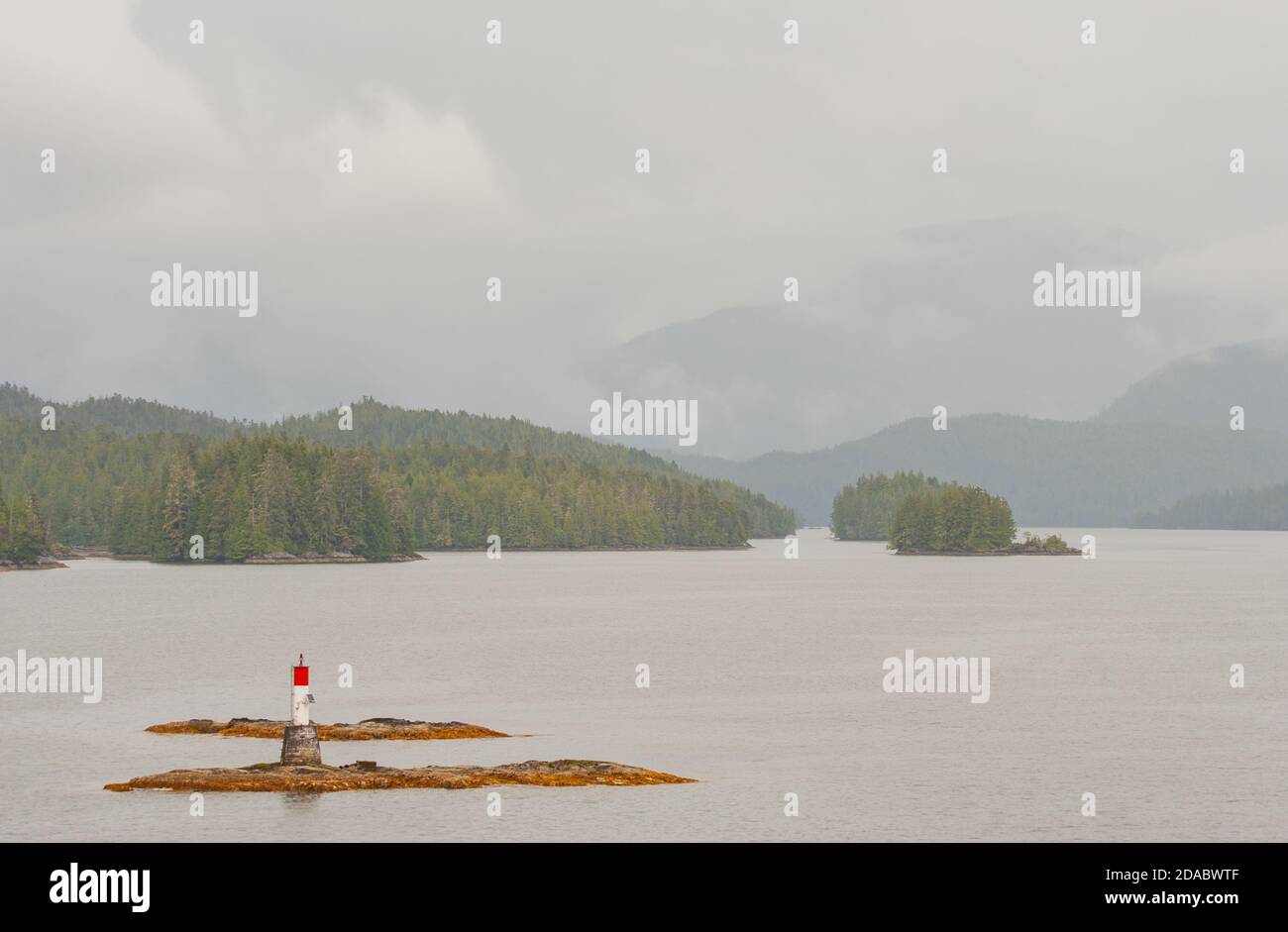 Vista panoramica dal traghetto al passaggio interno dell'isola di Vancouver. In primo piano una roccia con un faro. Sullo sfondo isole boscose e montagne. Foto Stock