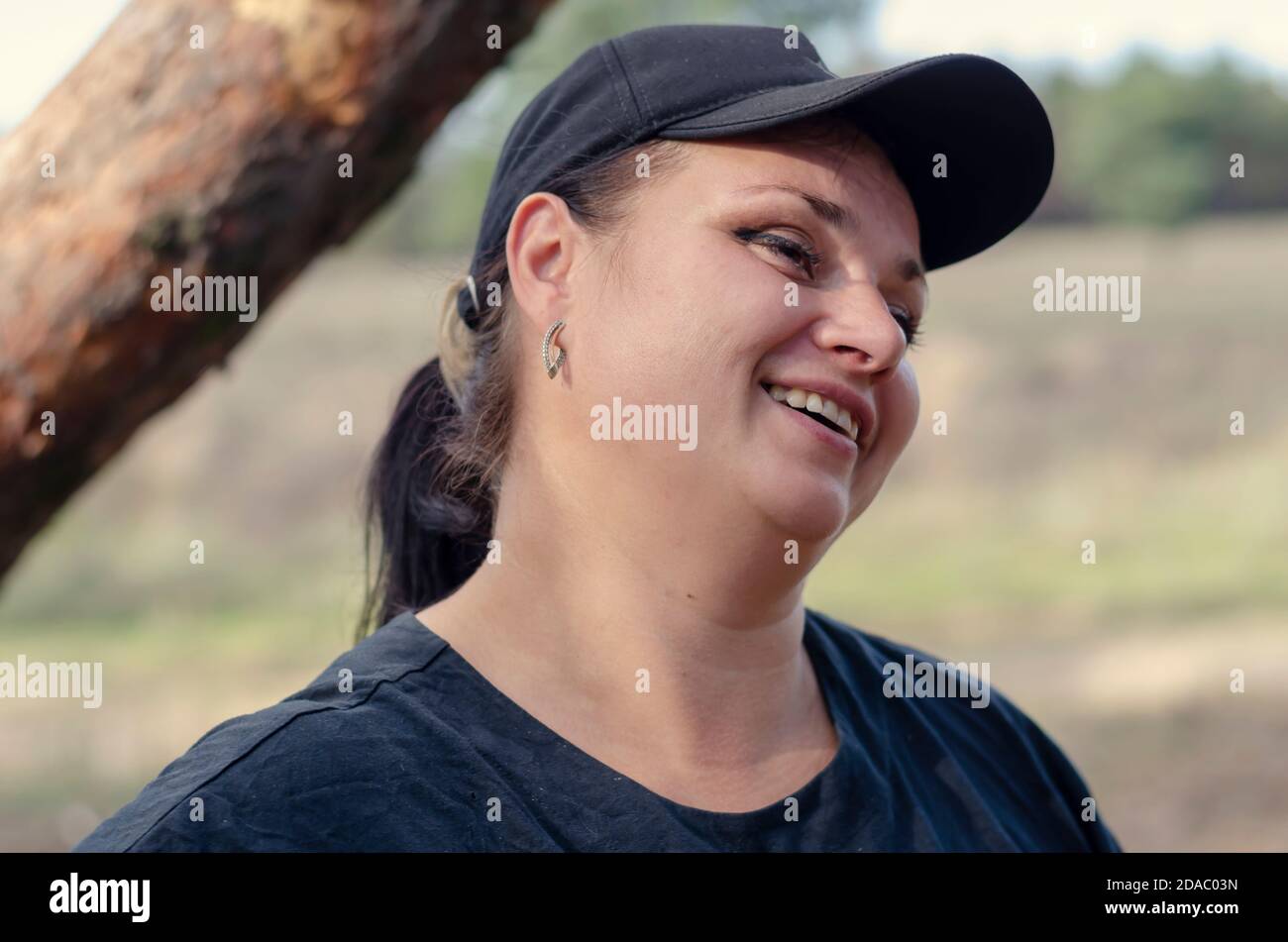 Ritratto di una donna armena allegra adulta che indossa un cappello da baseball nero e una camicia. Una donna di mezza età felice all'aperto. Foto Stock