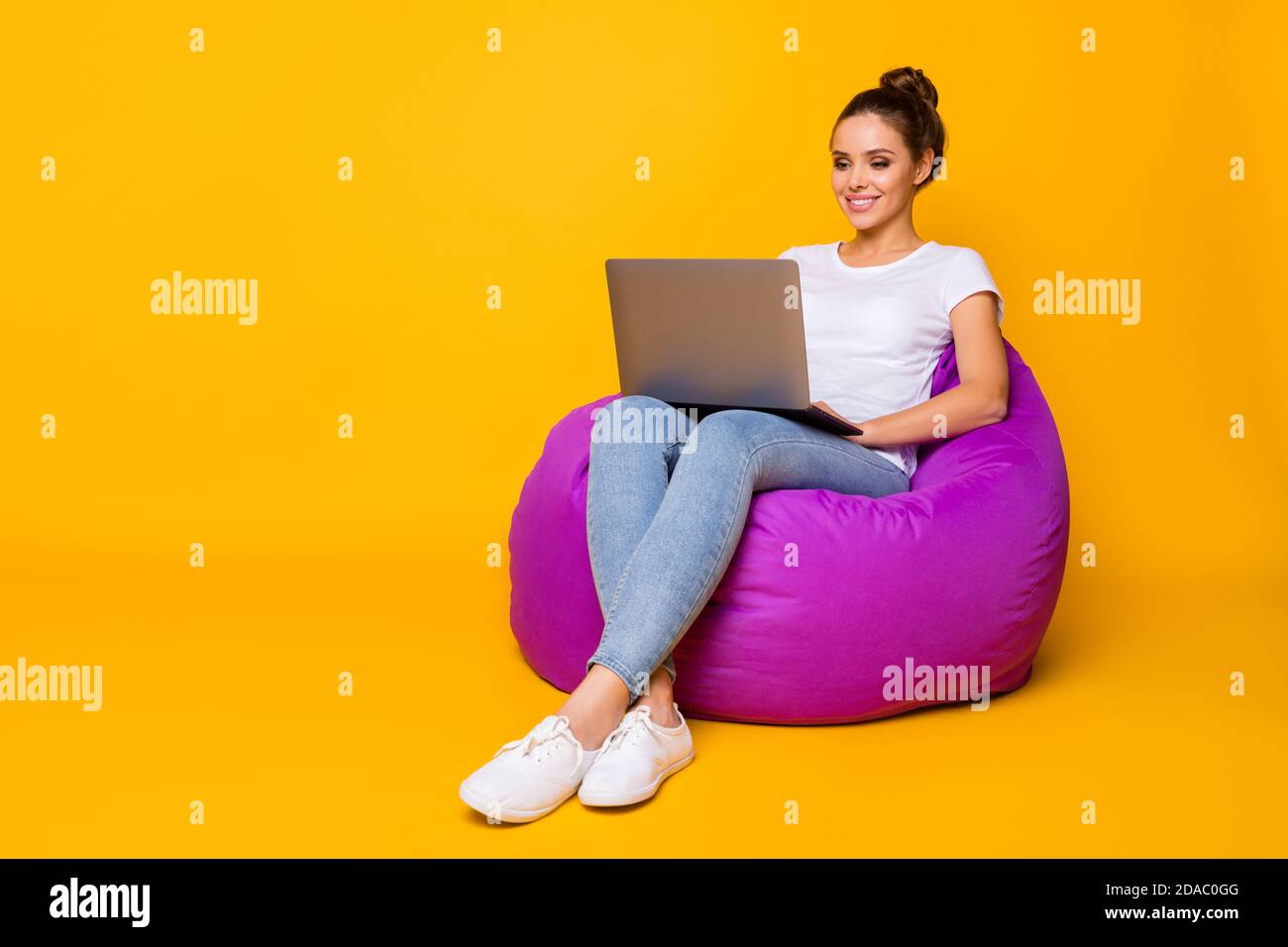 Foto corpo pieno di positivo ragazza allegra seduta borsa viola poltrona usa computer leggi e-book indossare scarpe bianche t-shirt isolato brillantezza Foto Stock