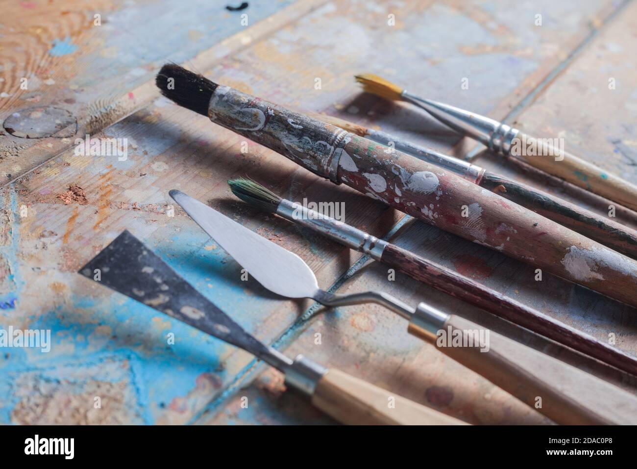 Varie spazzole e coltelli pallete. La scrivania in legno è coperta con belle vernici di diversi colori. Foto Stock