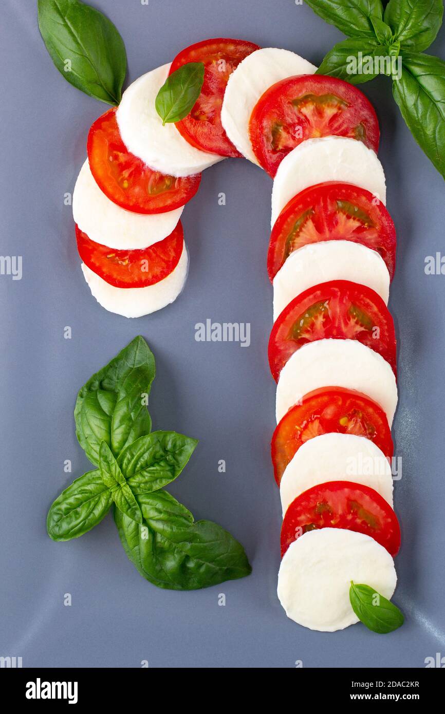 Insalata caprese di Natale sotto forma di canna caramella. Mozzarella e pomodoro su piatto grigio serviti per Capodanno sullo sfondo Foto Stock