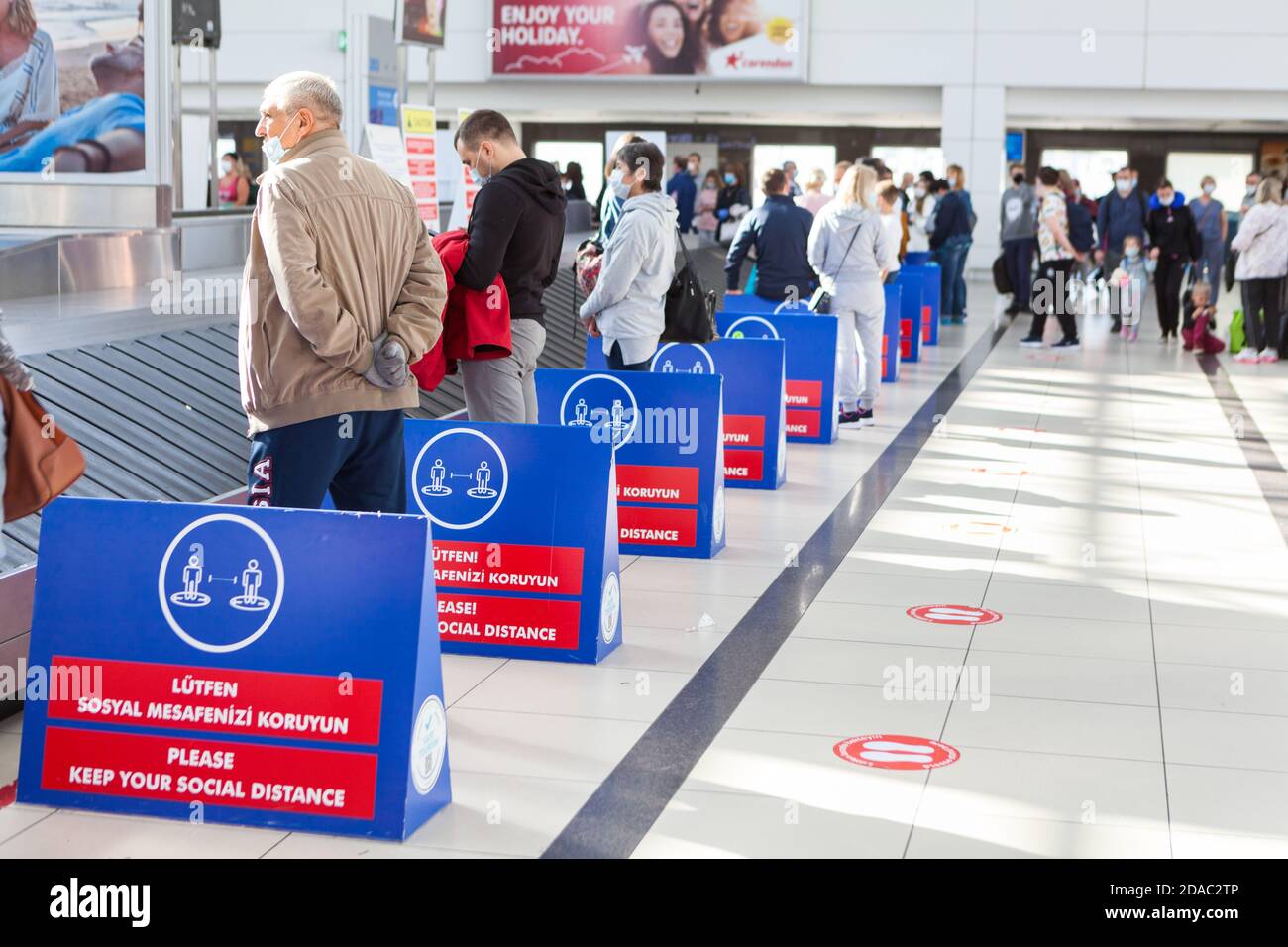 Antalya, Turchia-circa ottobre 2020: I passeggeri sono in attesa di bagagli senza mantenere una distanza sociale. Bacheche di avviso che chiedono loro di mantenere un dist sociale Foto Stock