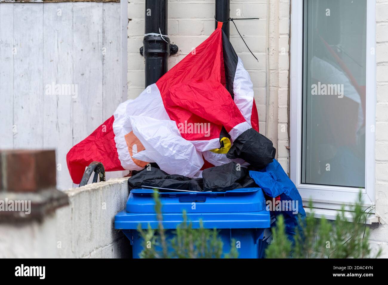 Sgonfia il Padre Natale su un bidone dei rifiuti. Babbo Natale decorazione esterna andato piatto su cestino rifiuti. Natale 2020 definito. Grande delamiamo Foto Stock