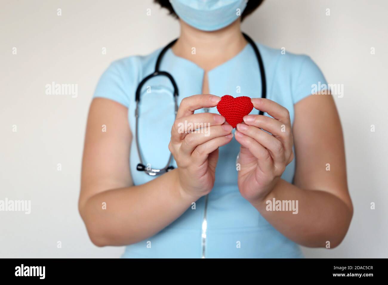 Salvare vite durante una pandemia di coronavirus covid-19, donna medico in maschera medica tenendo rosso cuore lavorato in mano Foto Stock