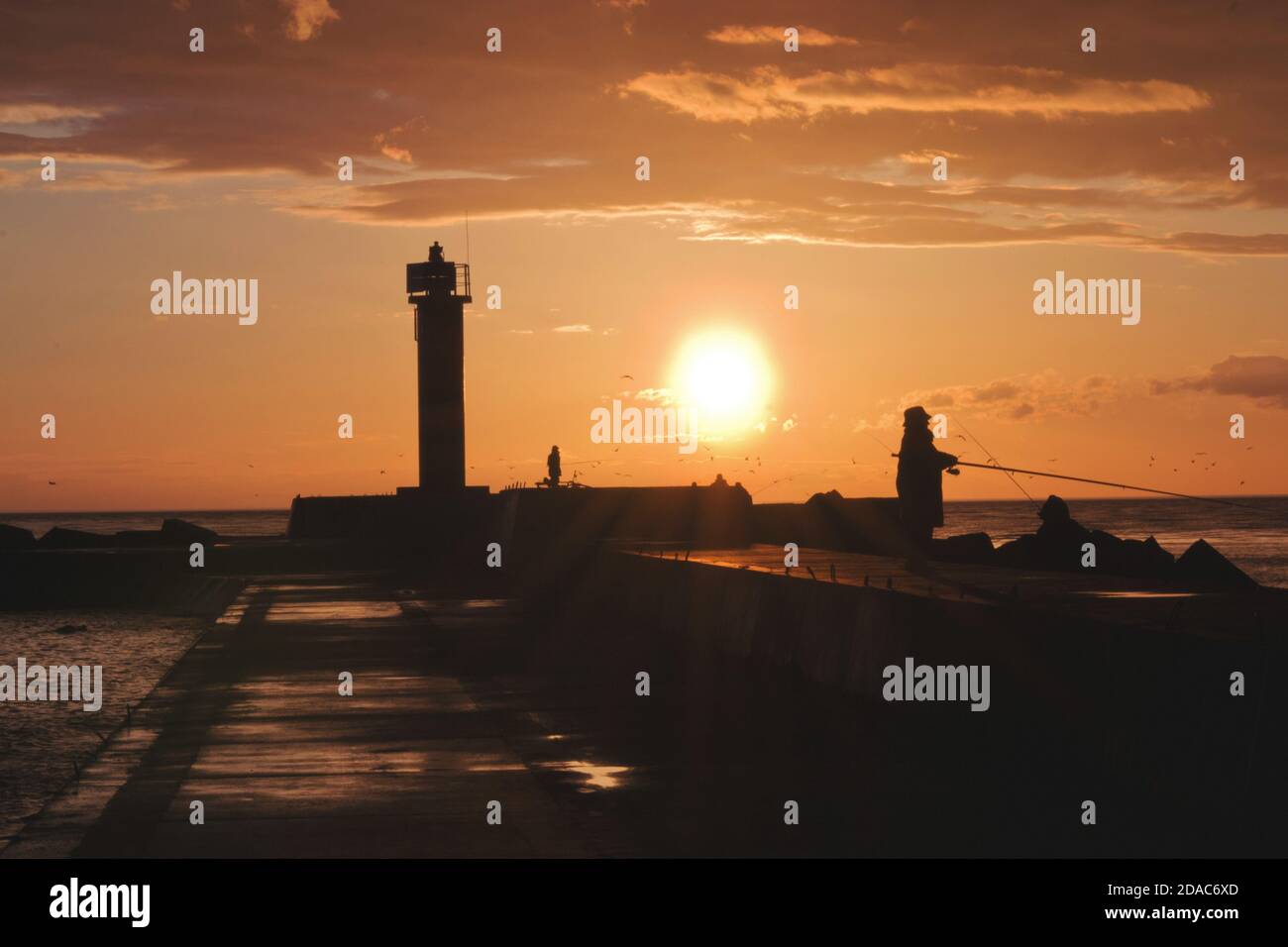 Vista del tramonto con silhouette di donne anziane che pescano al baltico Mare sul molo di Mangalsala a riga Foto Stock