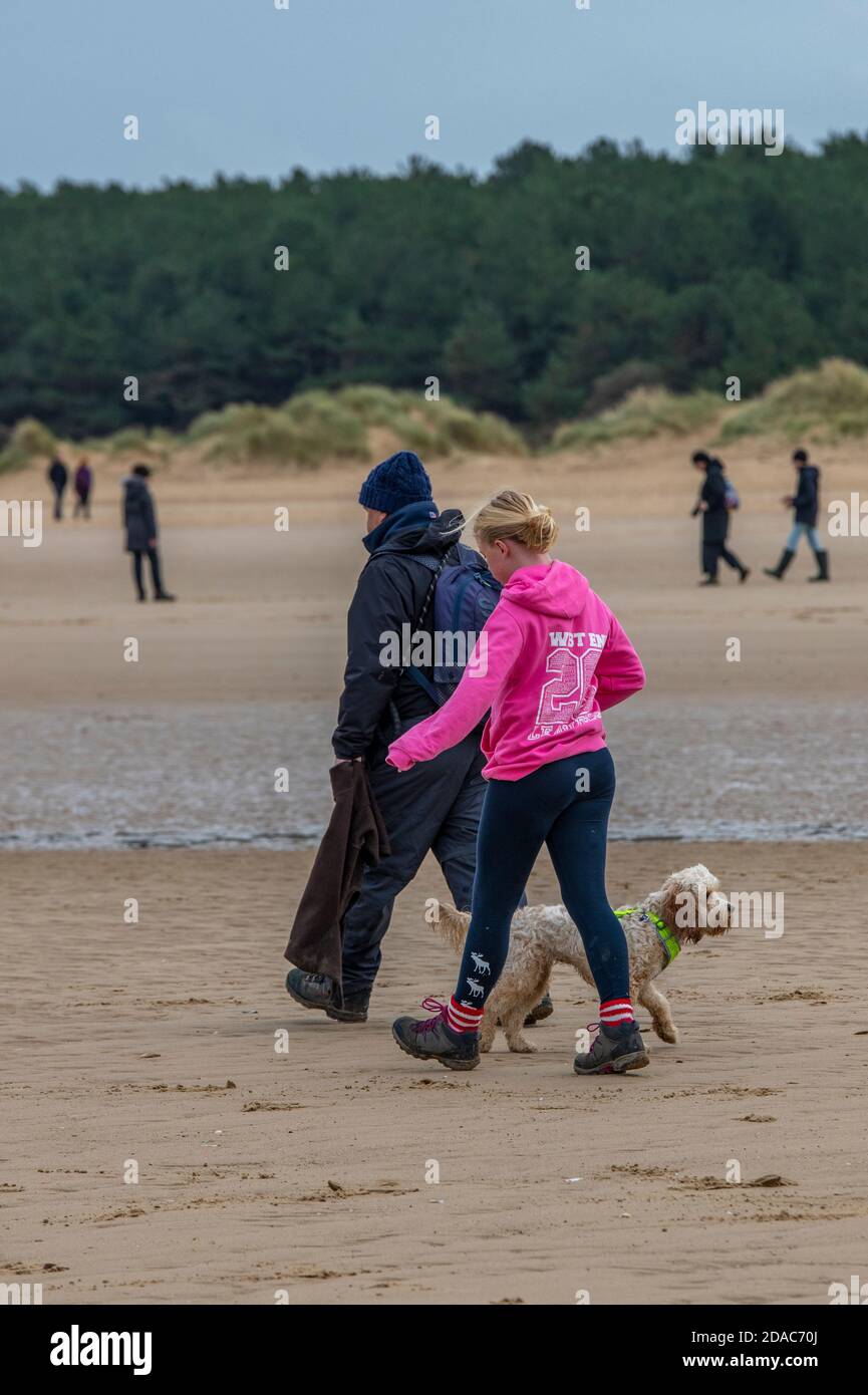 un uomo e una donna papà e una figlia che camminano un cane sulla spiaggia di norfolk su una spiaggia di sabbia a holkham. Foto Stock