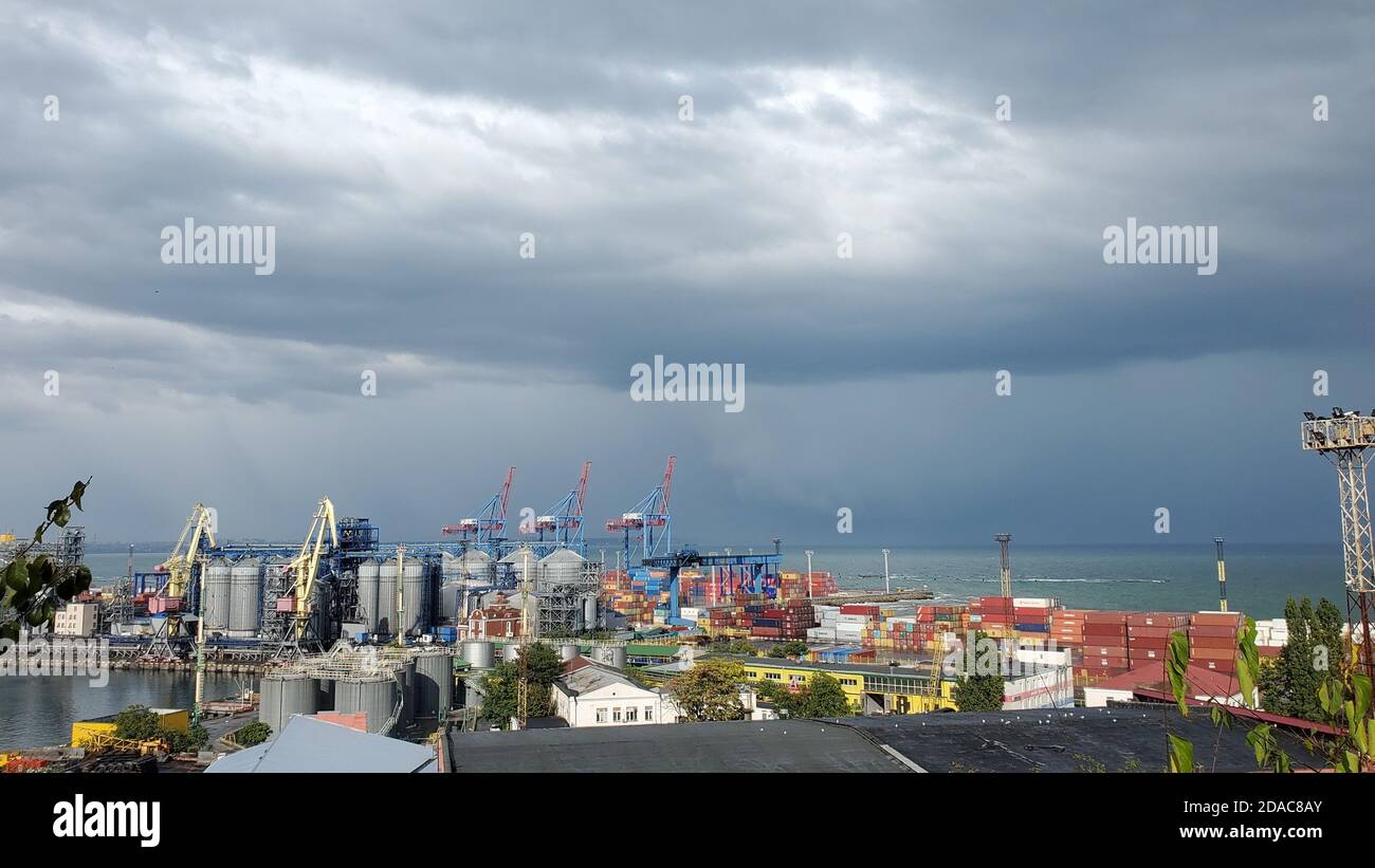 Porta con elevatori granella e area contenitore impilato. Vista sul mare industriale sotto le nuvole tempestose nel cielo alto. Paesaggio marittimo nel porto d'Europa Foto Stock