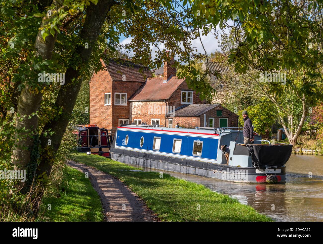 una chiatta di canale o una barca stretta che passa sotto alcuni alberi sul canale di grand union a braunston, northamptonshire, uk Foto Stock