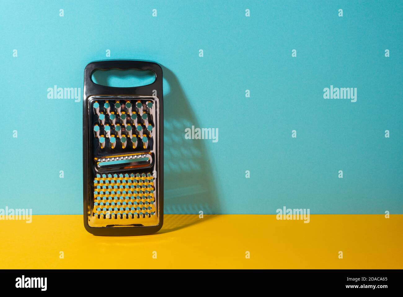 Grattugia in acciaio inox con manico in plastica su giallo e blu sfondo Foto Stock