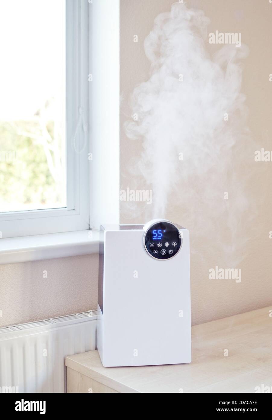 Umidificatore dell'aria con vapore sul tavolo vicino a. finestra e  radiatore di riscaldamento in soggiorno o camera da letto Foto stock - Alamy