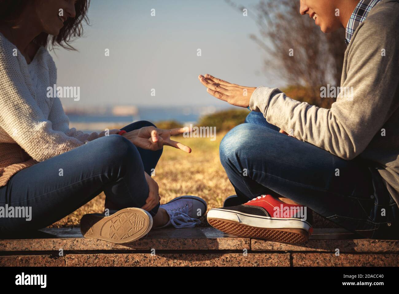 Primo piano di giovani coppie di ragazzi che giocano a rock carta forbici gioco seduta insieme all'aperto. Foto Stock