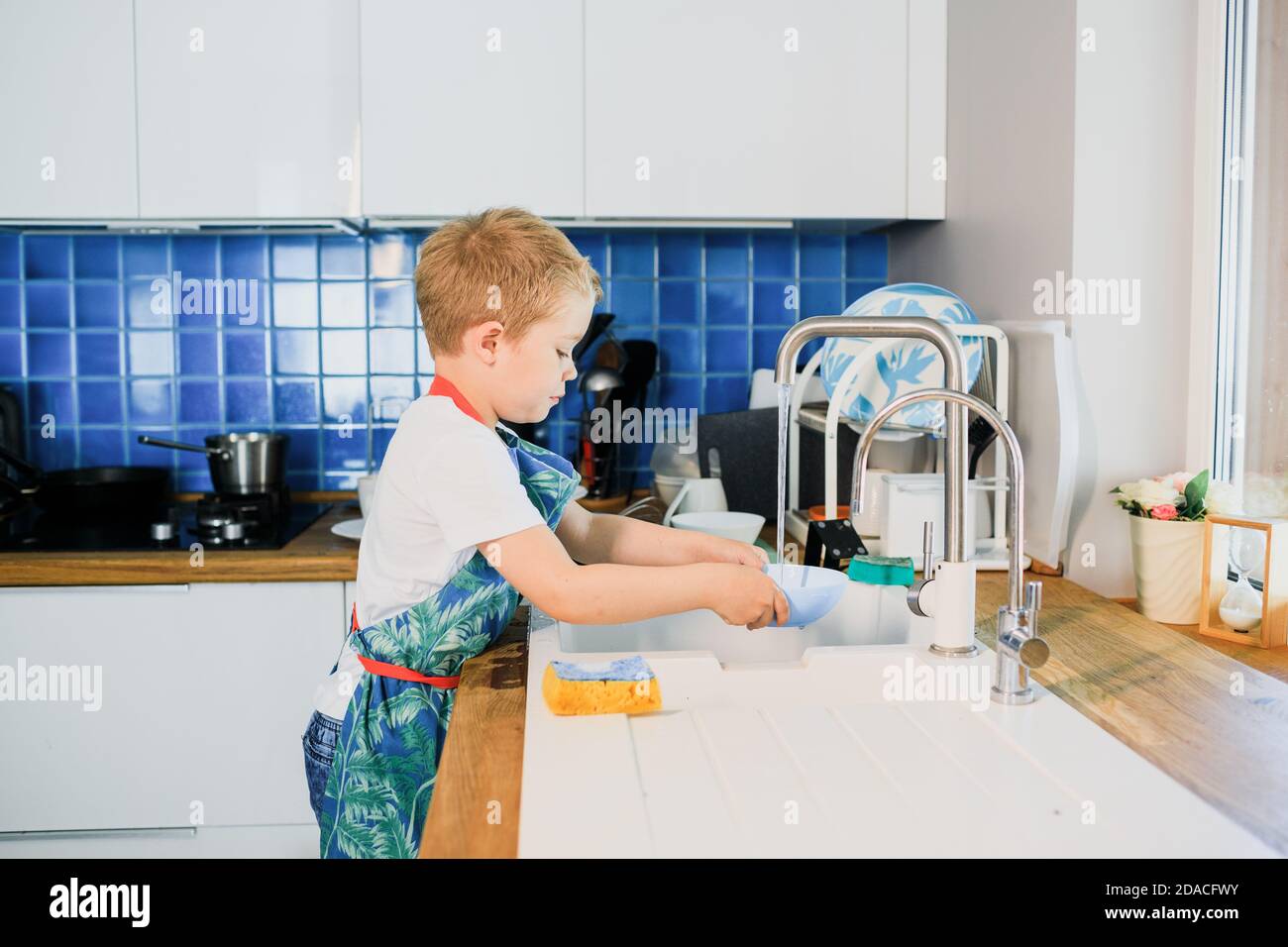 un ragazzino lava i piatti in una cucina moderna Foto Stock