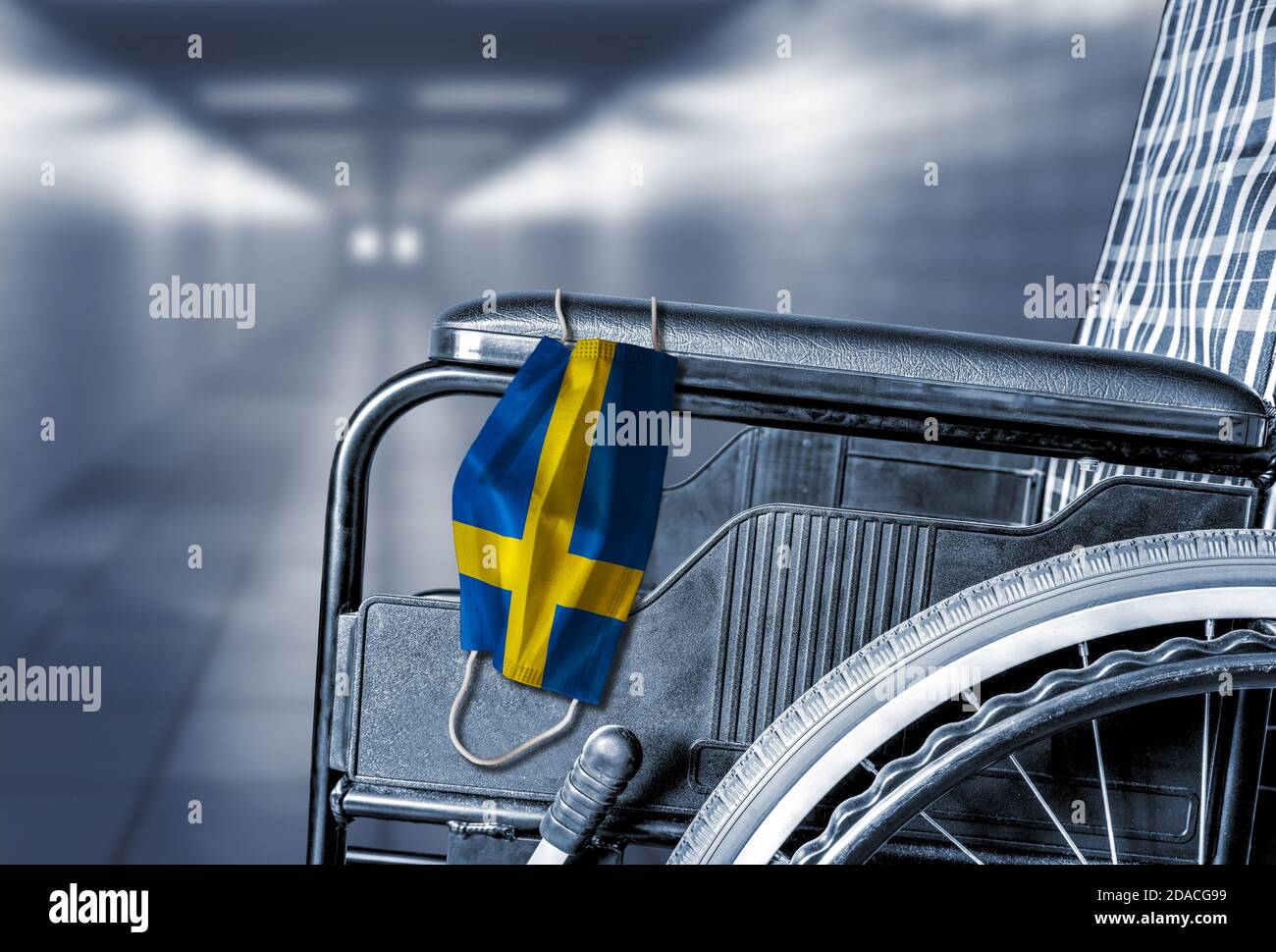 Bandiera di Svezia sulla maschera facciale appesa su sedia a rotelle vuota nel corridoio dell'ospedale o della casa di cura di pensione con spazio di copia. Concetto di COVID-19 pa Foto Stock