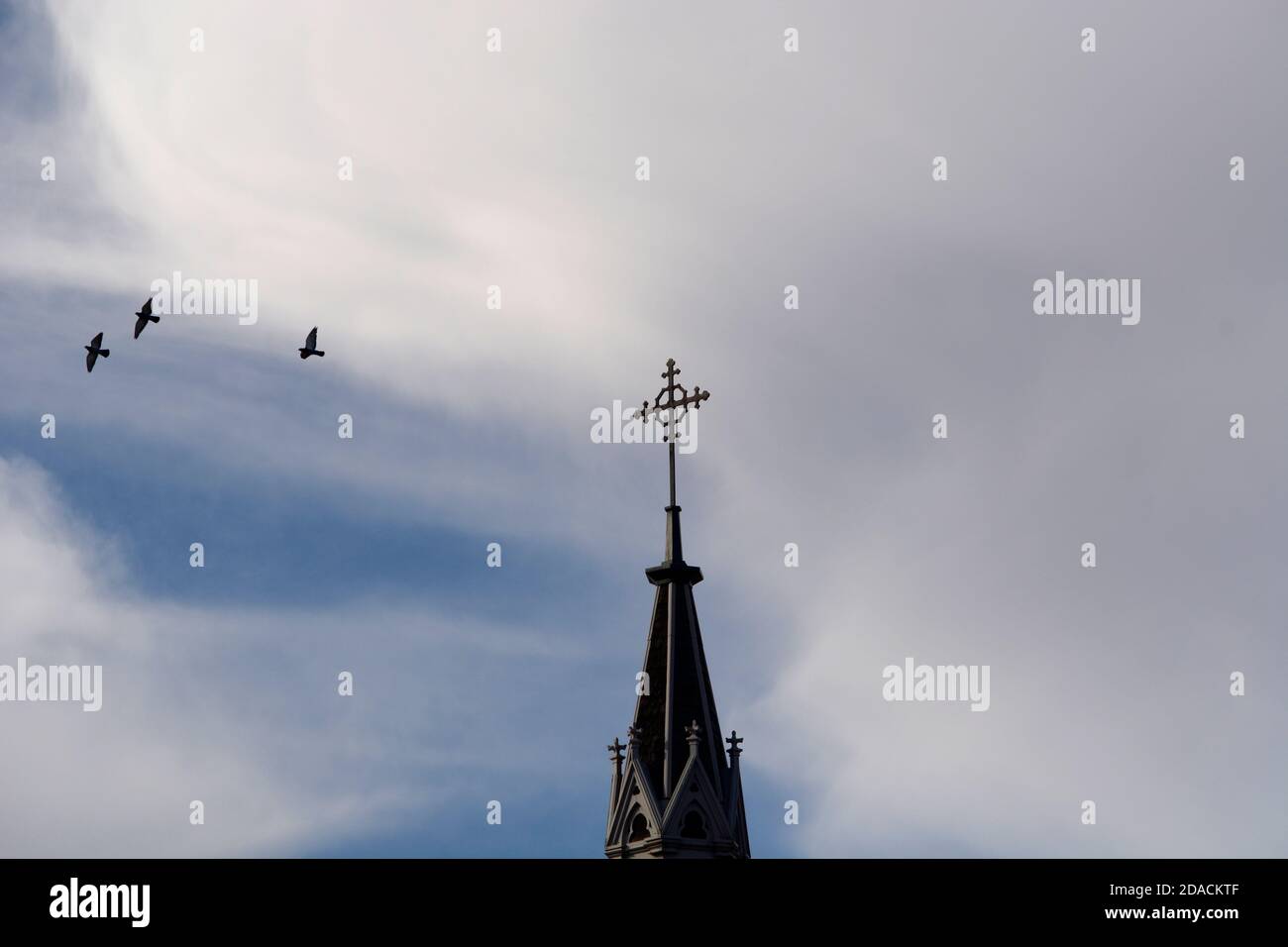 I piccioni volano intorno alla croce cristiana in metallo in cima alla storica Cappella Loretto a Santa Fe, New Mexico. Foto Stock