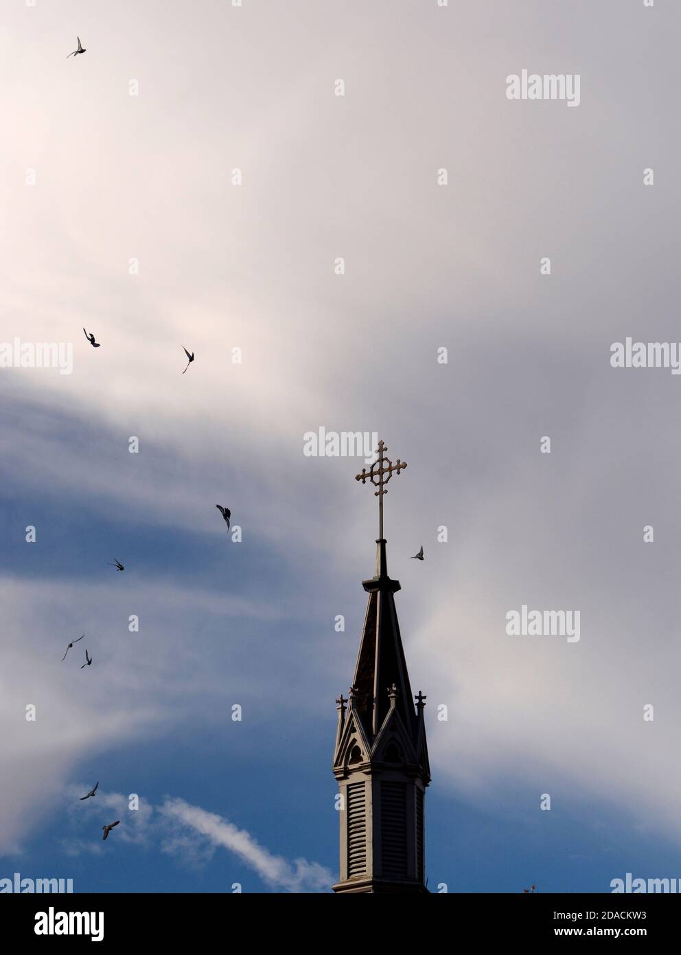 I piccioni volano intorno alla croce cristiana in metallo in cima alla storica Cappella Loretto a Santa Fe, New Mexico. Foto Stock