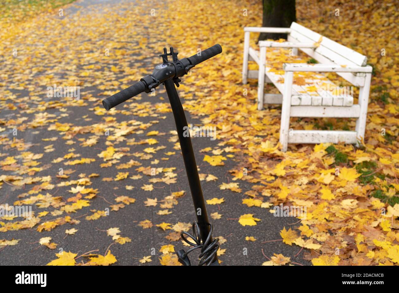 Uno scooter davanti a una panchina coperta di fogliame giallo d'autunno. Concetto, riposo, vacanza, solitudine. Foto di alta qualità Foto Stock