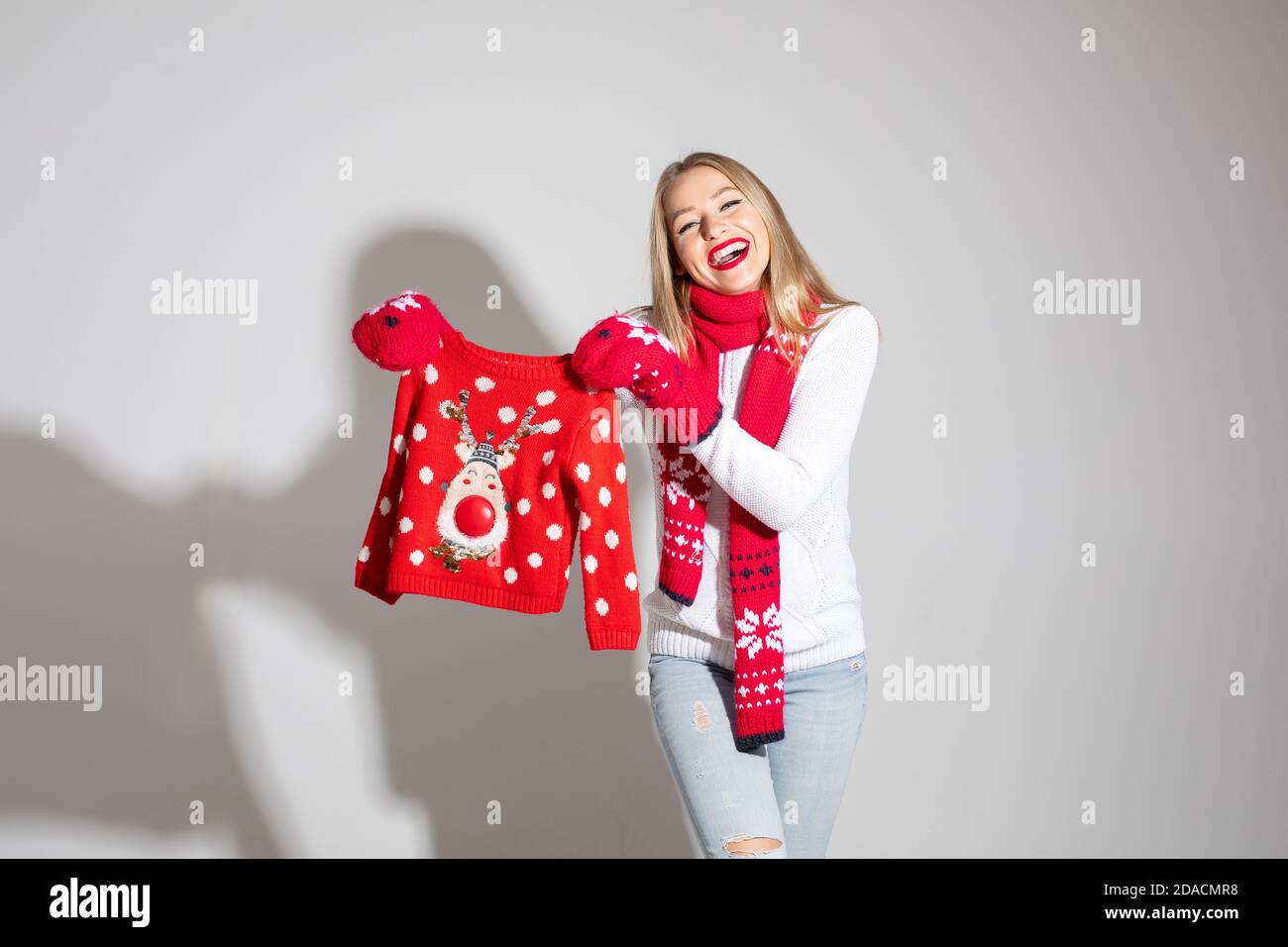 donna attraente in pullover bianco, sciarpa rossa e guanti rossi con design natalizio contiene il pullover rosso Foto Stock