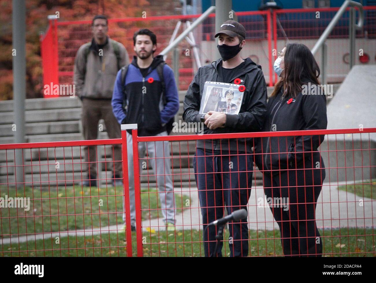 Vancouver, Canada. 11 Nov 2020. Un residente porta una foto mentre guarda la cerimonia del giorno della memoria dietro la recinzione a Victory Square a Vancouver, British Columbia, Canada, 11 novembre 2020. A causa della pandemia di COVID-19, la Giornata della memoria di quest'anno si è svolta nell'ambito di misure di sicurezza sanitaria. La Piazza della Vittoria è stata chiusa al pubblico e ha consentito solo a un numero limitato di partecipanti di partecipare alla cerimonia. Credit: Liang Sen/Xinhua/Alamy Live News Foto Stock