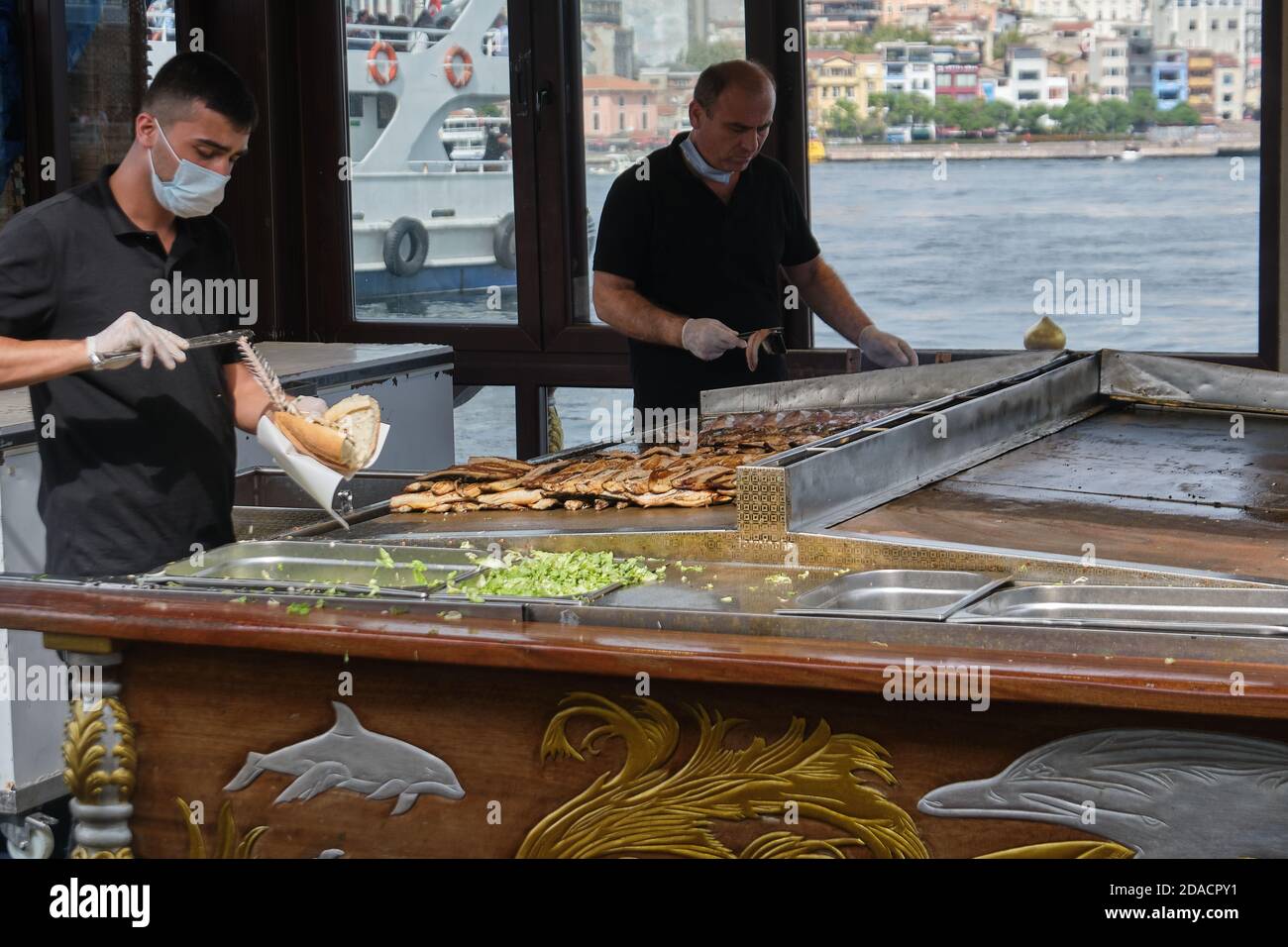 Il personale indossa maschere che cucinano Balik Ekmek su una barca nel porto di Eminonu, Istanbul, Turchia Foto Stock